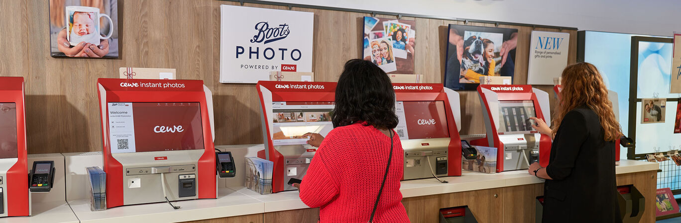 Three people using photo kiosks at Boots Photo to create memories